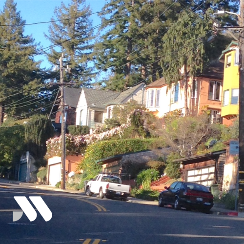 Residential homes along a tree-lined hillside street in Berkeley, California with mature landscaping and established East Bay neighborhoods.