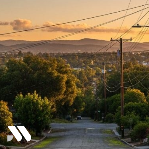 Residential street in Crockett, California surrounded by mature trees, utility lines, and scenic East Bay hillside views at sunset.